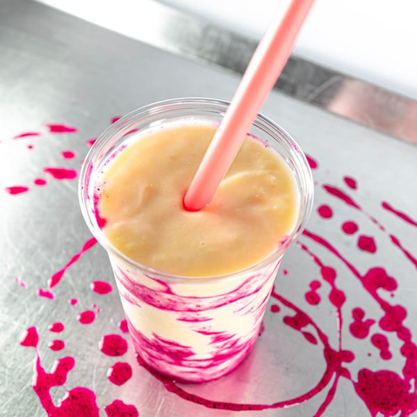 A Superfood Cafe smoothie with yellow and pink swirls, a pink straw, and pink splatters.