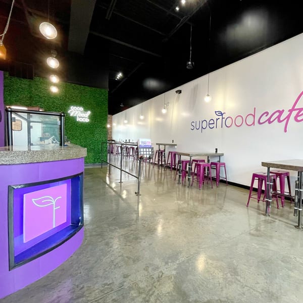 Interior of Superfood Cafe with a purple counter, green wall, and pink stools at tables.