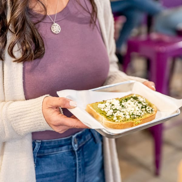A person holds a metal tray with a slice of avocado toast topped with feta cheese.