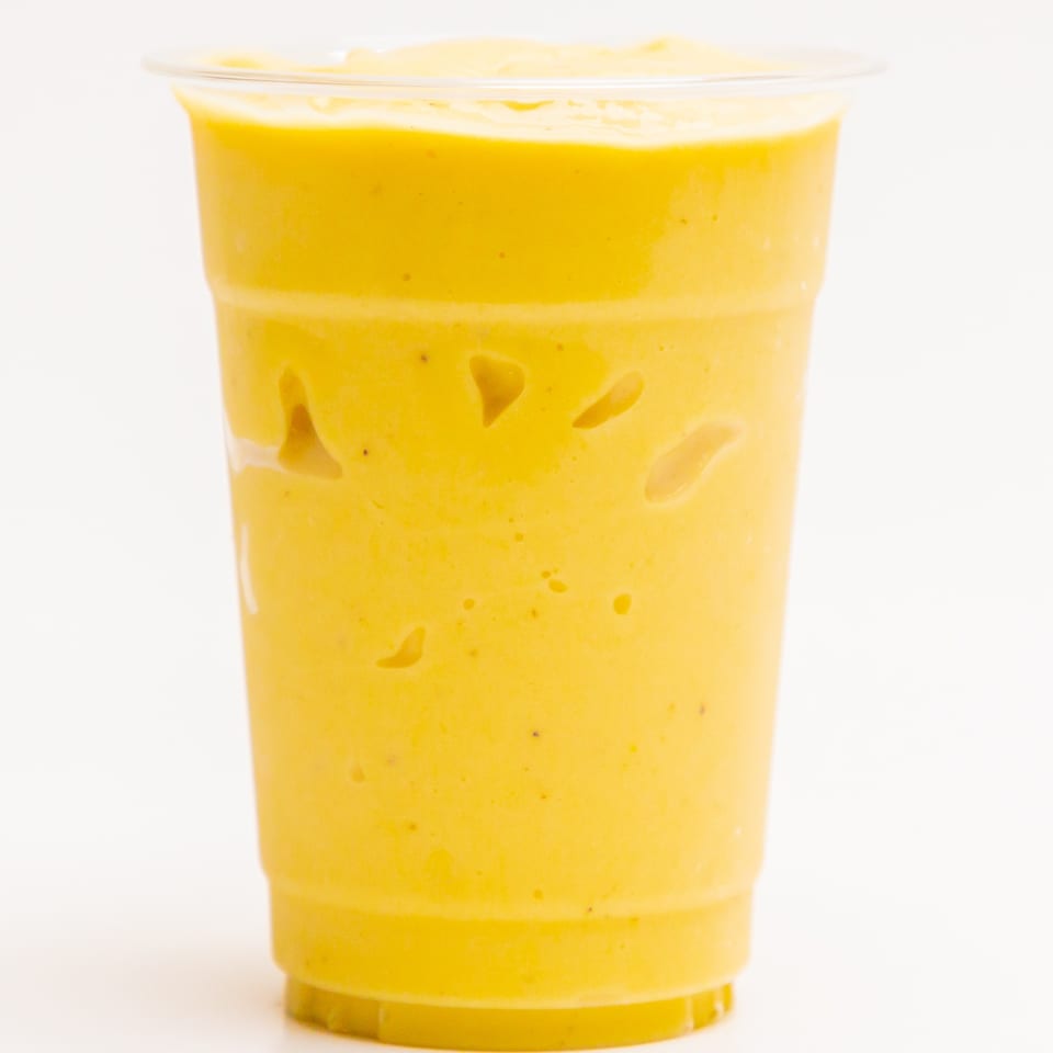 A vibrant yellow Superfood Cafe smoothie in a clear plastic cup, against a white background.