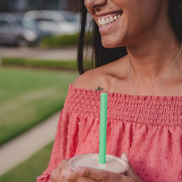 Smiling woman in a pink top holding a Superfood Cafe smoothie with a green straw outdoors.