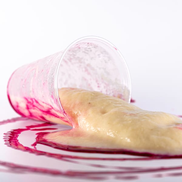 Spilled Superfood Cafe smoothie, yellow and pink, oozing from a clear cup onto a white surface.