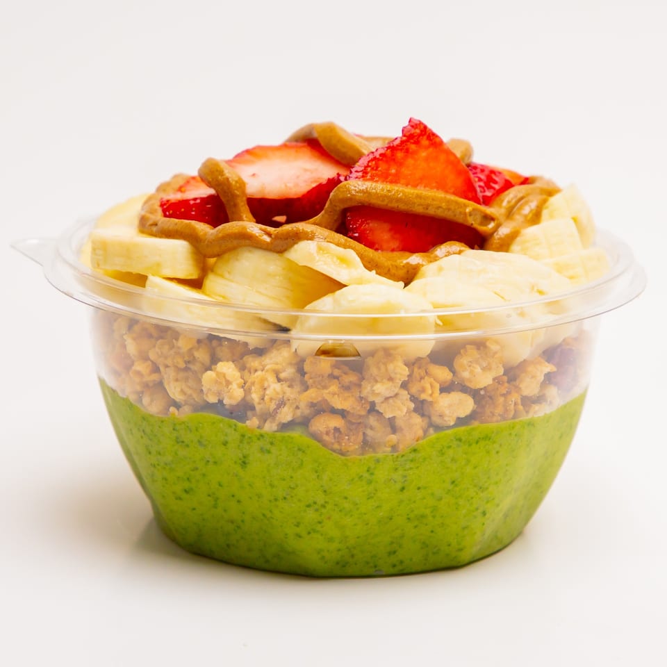 A Superfood Cafe green smoothie bowl with granola, bananas, strawberries, and peanut butter drizzle.