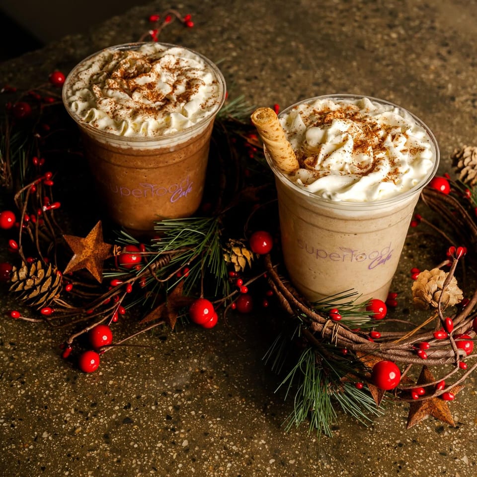Two Superfood Cafe smoothies with whipped cream and cinnamon, surrounded by a festive wreath.