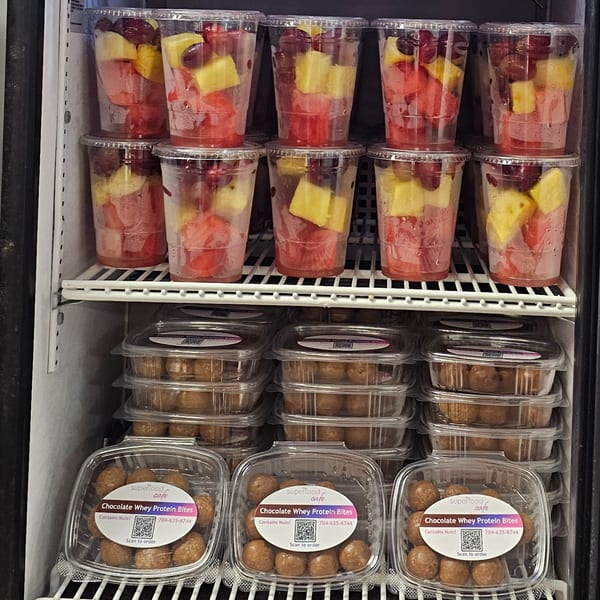 A Superfood Cafe fridge filled with fruit cups and containers of Chocolate Whey Protein Bites.