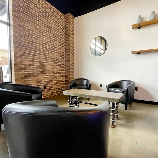 Cozy seating area with black armchairs, a concrete table, brick wall, and decorative shelves.