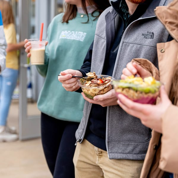 Customers at Superfood Cafe holding healthy smoothie bowls and a drink with a red straw.