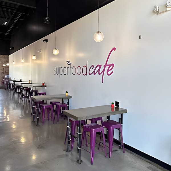 Interior of Superfood Cafe with purple stools, high-top tables, and the cafe's logo on a white wall.