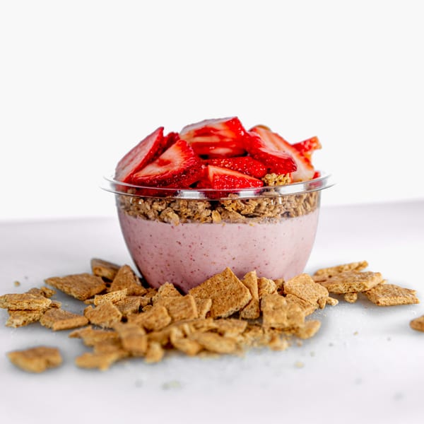 Strawberry smoothie bowl with granola and fresh strawberries, surrounded by cereal pieces.