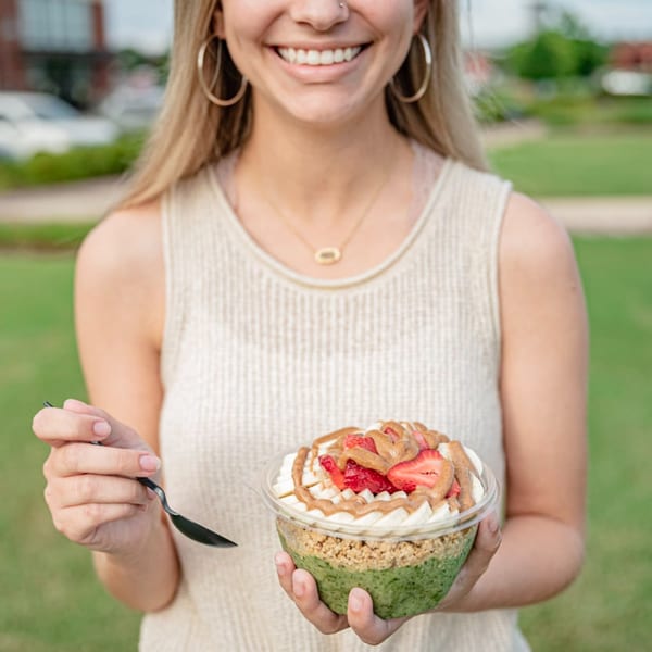Smiling woman holding a Superfood Cafe green smoothie bowl topped with strawberries and peanut butter.
