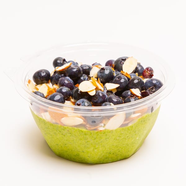 Green smoothie bowl topped with fresh blueberries and sliced almonds in a clear plastic container.