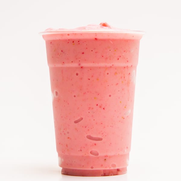 A pink strawberry smoothie in a clear plastic cup, filled to the brim, against a white background.