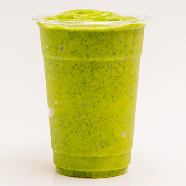 A vibrant green Superfood Cafe smoothie in a clear plastic cup, filled to the brim.