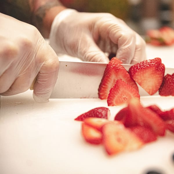 Gloved hands slicing fresh strawberries on a white cutting board at Superfood Cafe.